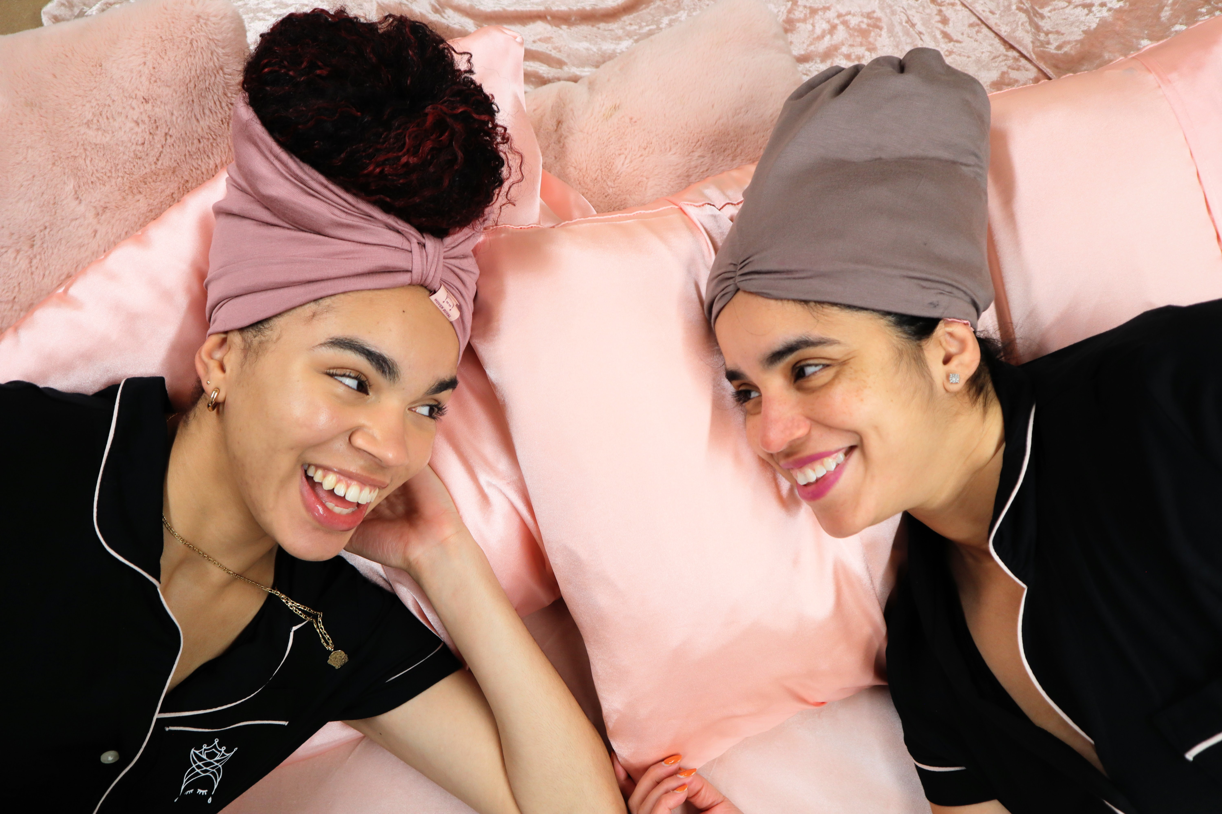 Two women lying on pink pillows wearing headscarves and pajamas.